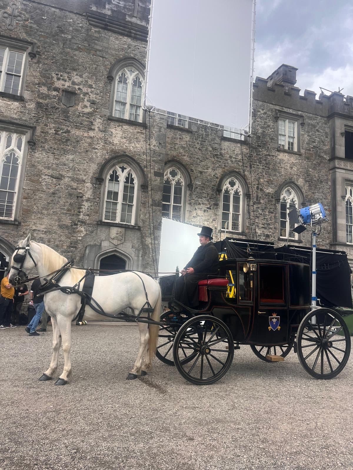 A white horse and black period carriage under film lighting at a castle