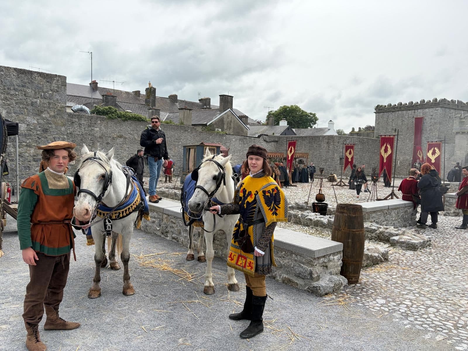 Costumed riders holding white horses on a castle set with banners flying