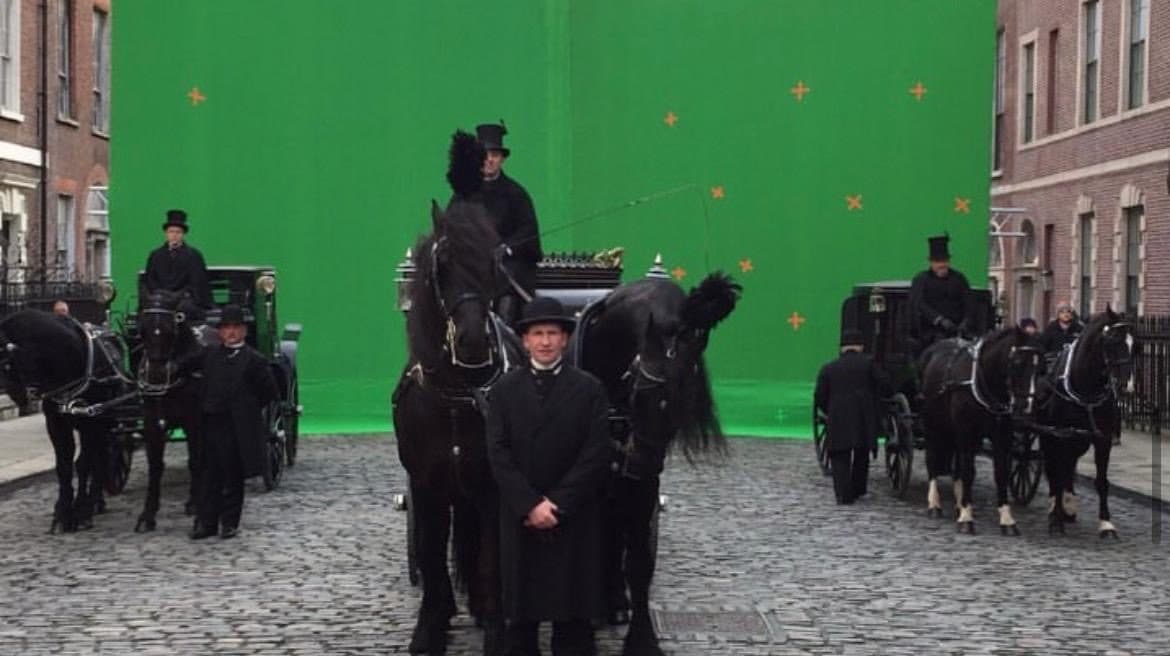 Black horses and period hearses lined up in front of a green screen