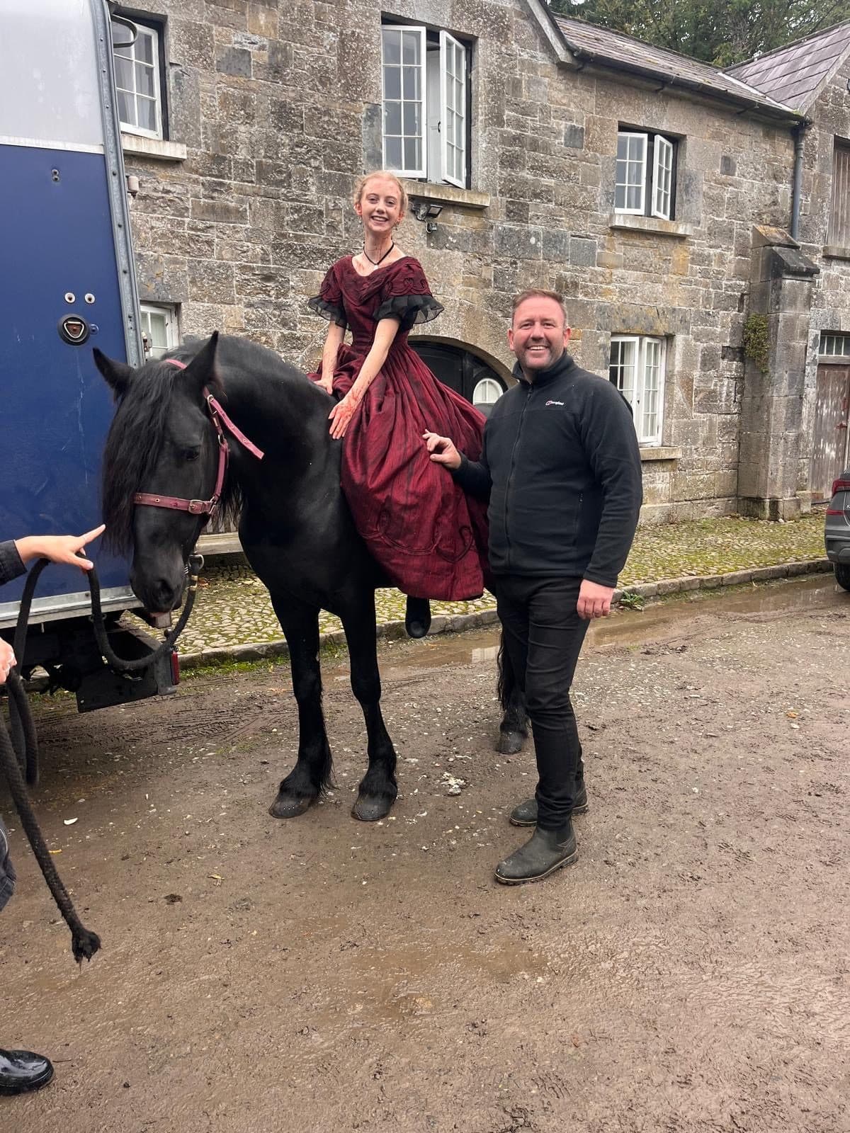 An actress in period costume mounted on a black Friesian, with David alongside