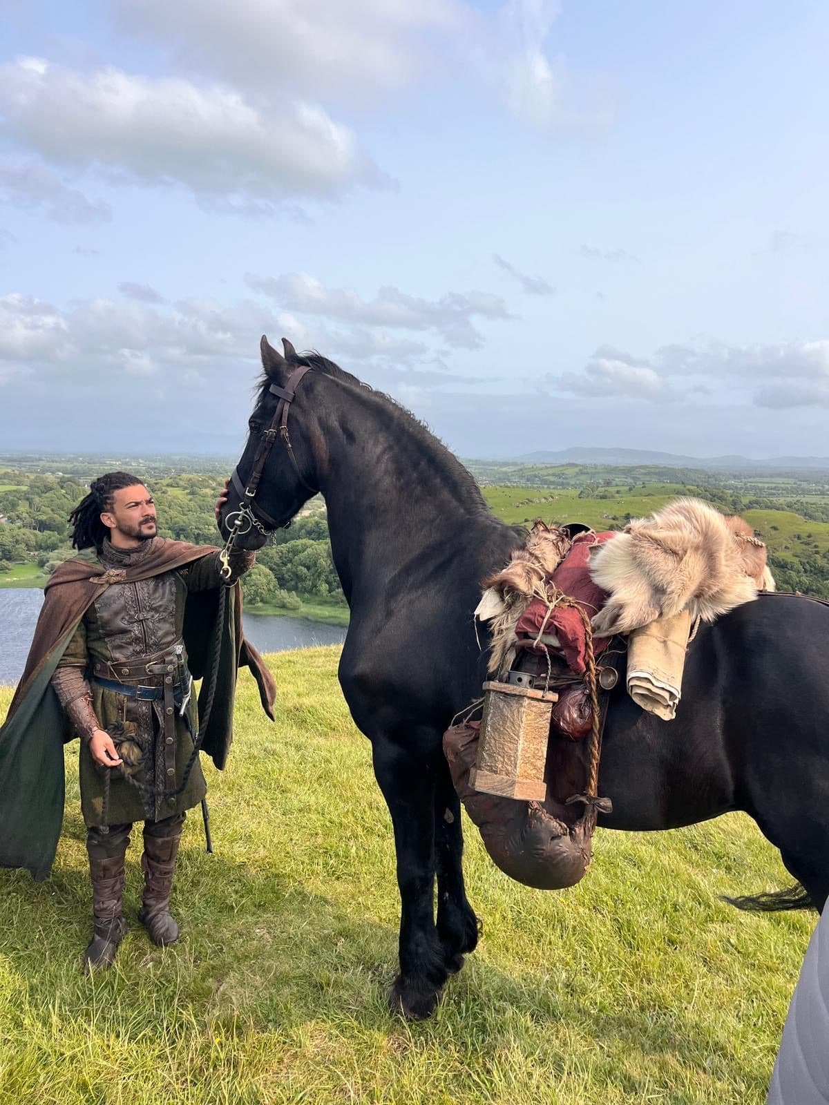 A costumed rider leading a black Friesian on an Irish hillside