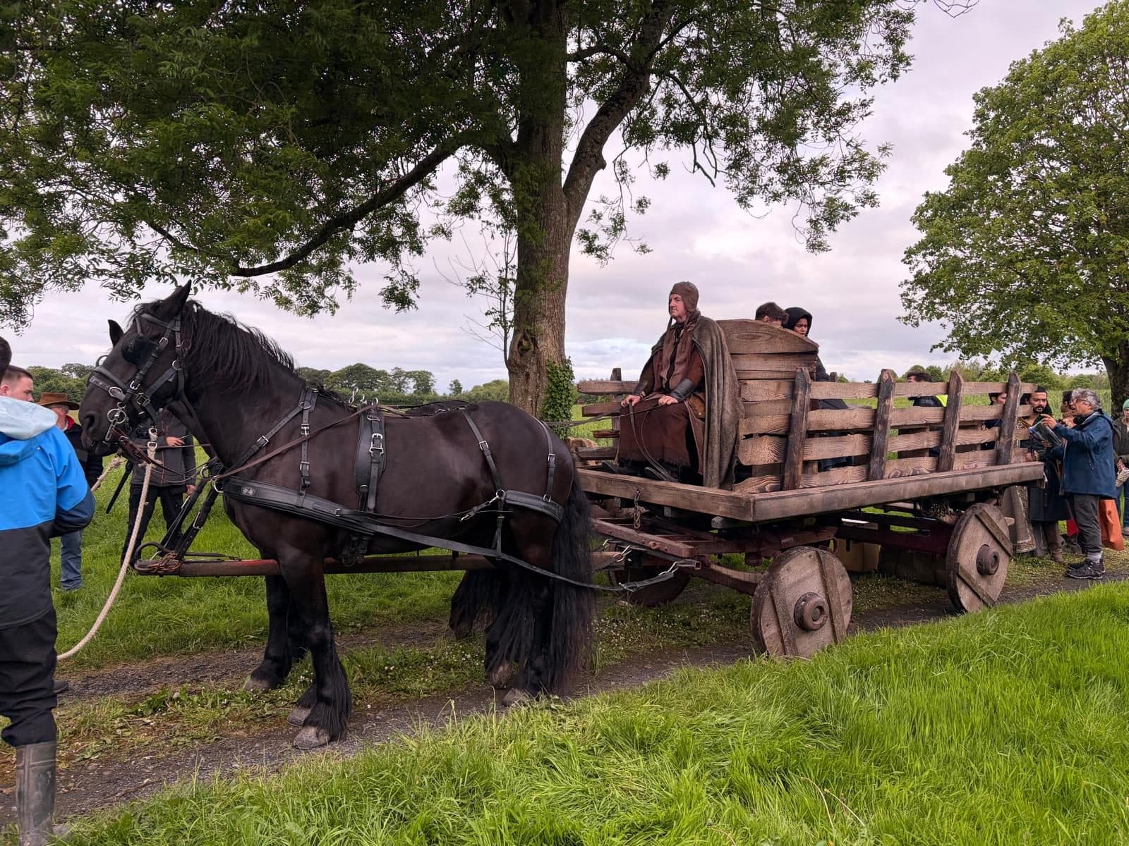 A black Friesian in harness to a period wagon, surrounded by crew between takes